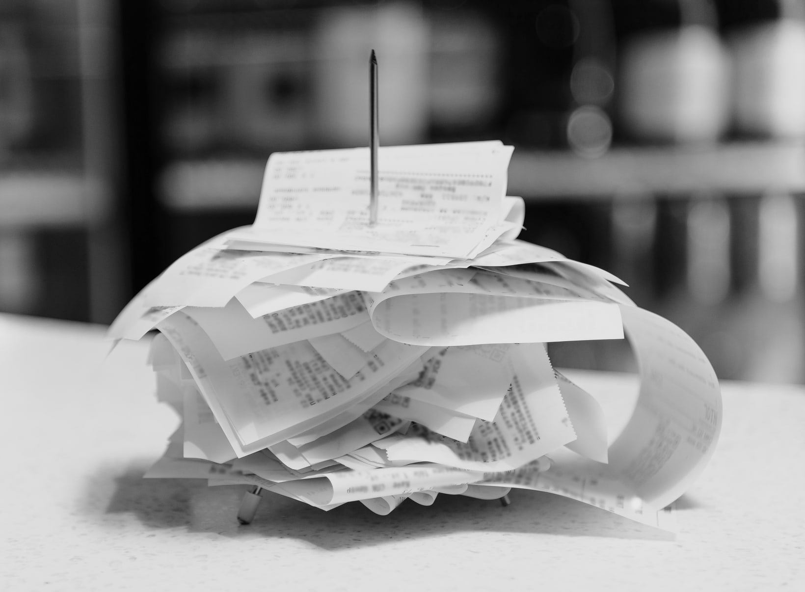 Paper receipts piled on a spike on a counter