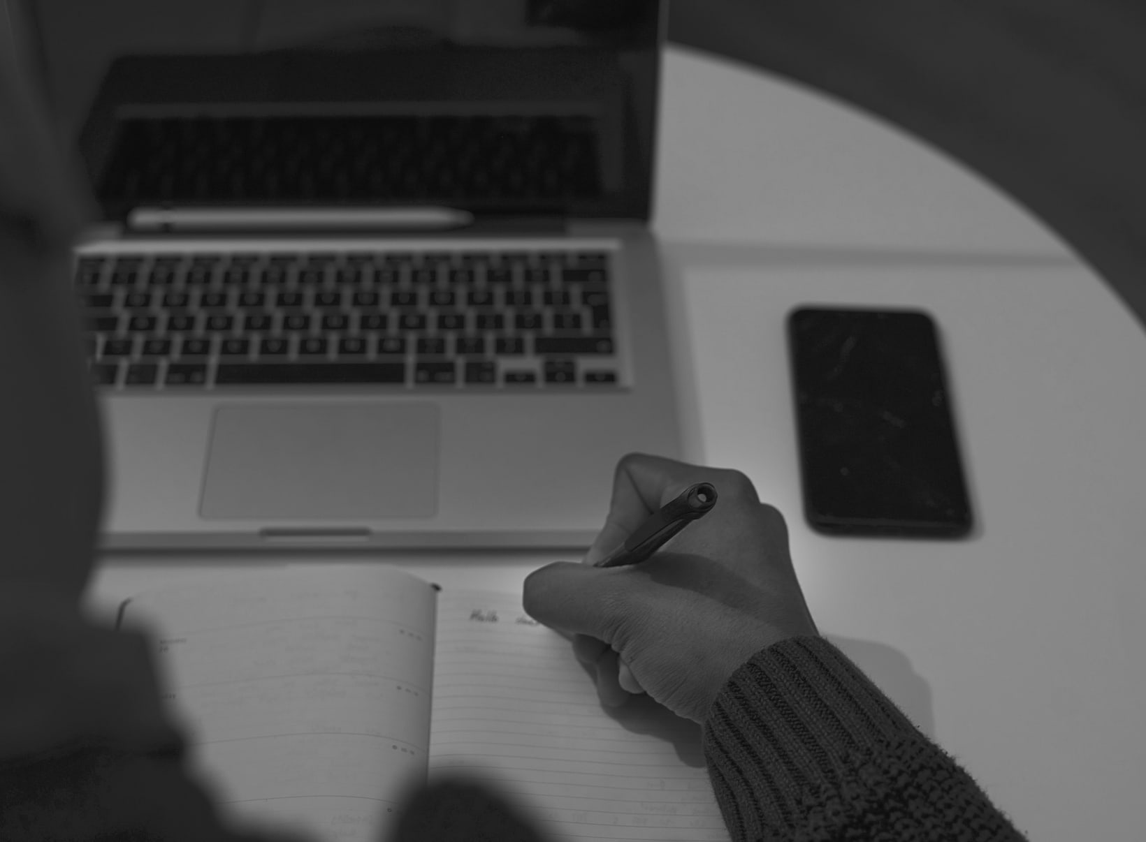 Hand writing notes in a planner beside a laptop